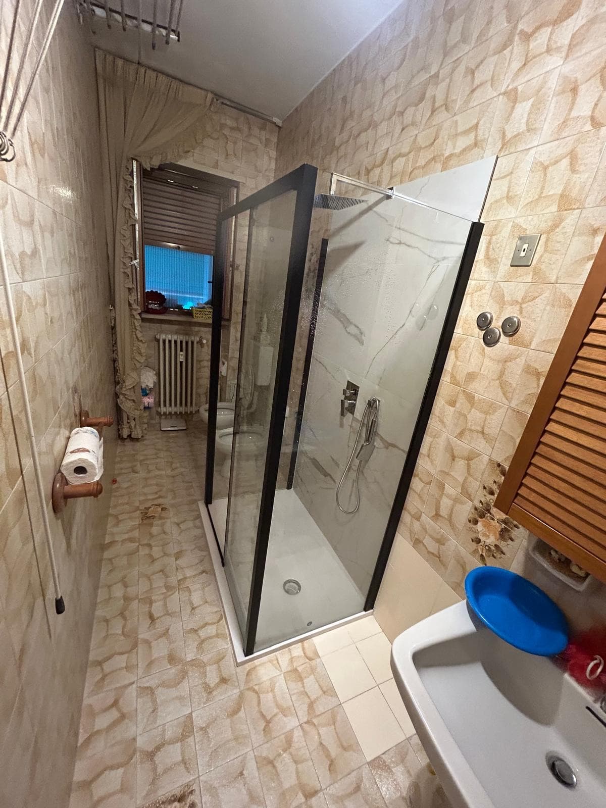 Box doccia con profili neri installato in un bagno con le piastrelle originali